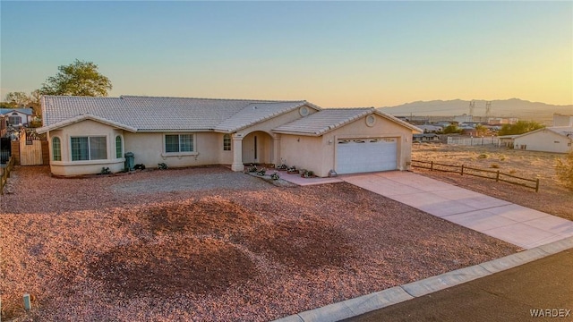 ranch-style home with an attached garage, a mountain view, a tile roof, fence, and driveway