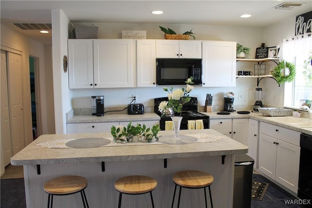 kitchen with visible vents, white cabinetry, a sink, black appliances, and a kitchen breakfast bar