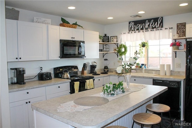 kitchen featuring recessed lighting, light countertops, white cabinets, black appliances, and a kitchen breakfast bar