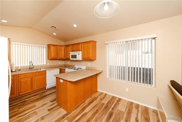 kitchen featuring visible vents, light wood-style flooring, a peninsula, white appliances, and a sink