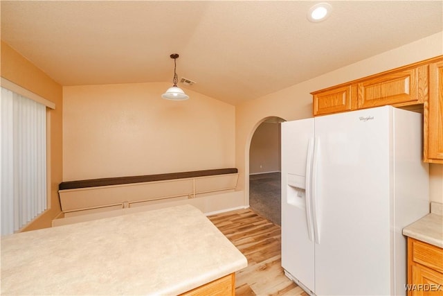 kitchen featuring light wood finished floors, pendant lighting, light countertops, vaulted ceiling, and white refrigerator with ice dispenser