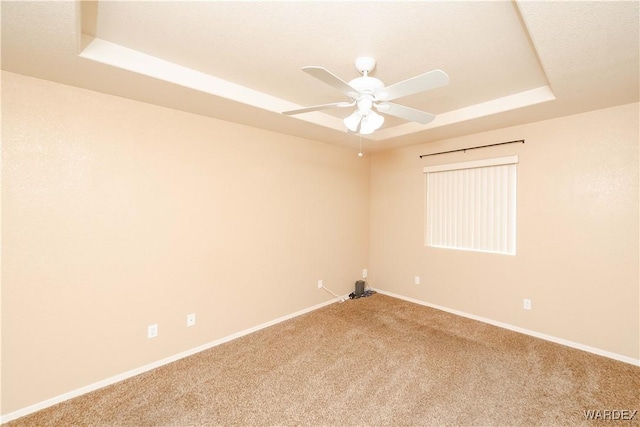 empty room with baseboards, carpet flooring, a ceiling fan, and a tray ceiling