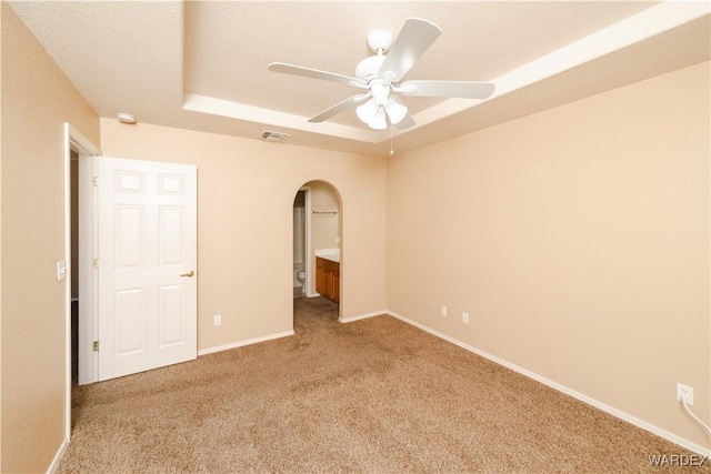 unfurnished bedroom featuring visible vents, baseboards, carpet flooring, arched walkways, and a raised ceiling