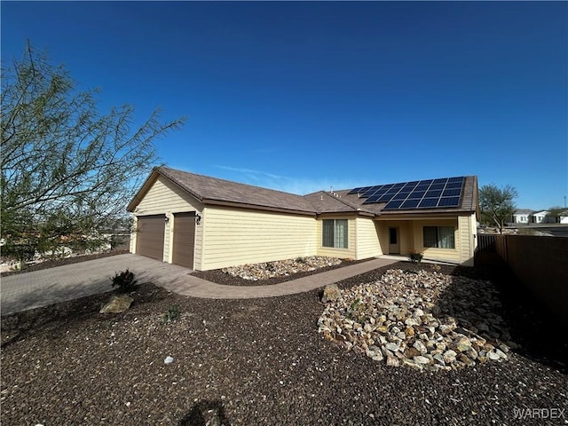 ranch-style house featuring solar panels, an attached garage, fence, and driveway