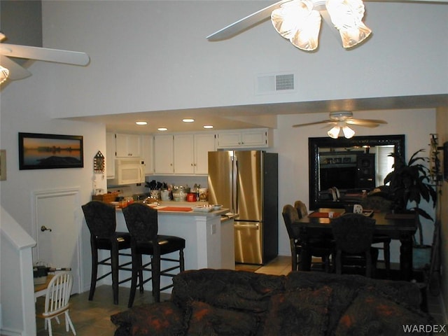 kitchen with white microwave, a peninsula, visible vents, white cabinets, and freestanding refrigerator