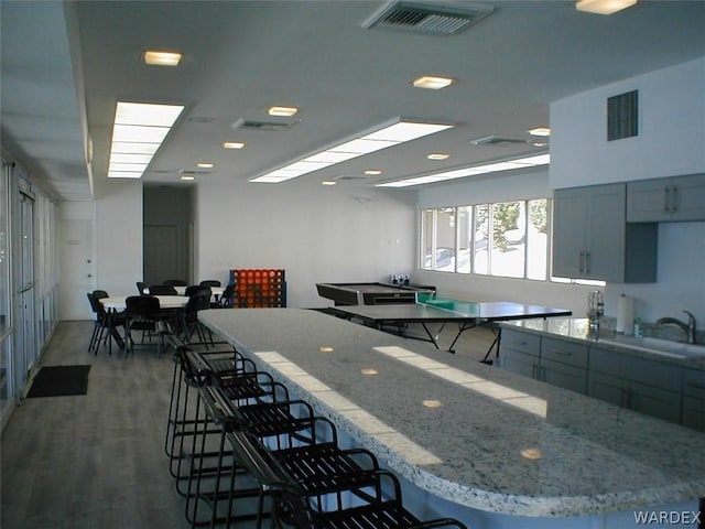 kitchen featuring wood finished floors, visible vents, a sink, and light stone countertops