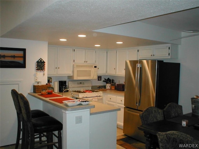 kitchen featuring recessed lighting, light countertops, white cabinetry, white appliances, and a peninsula