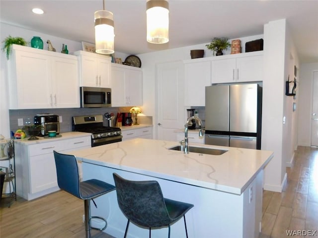 kitchen with decorative light fixtures, appliances with stainless steel finishes, white cabinetry, a sink, and an island with sink