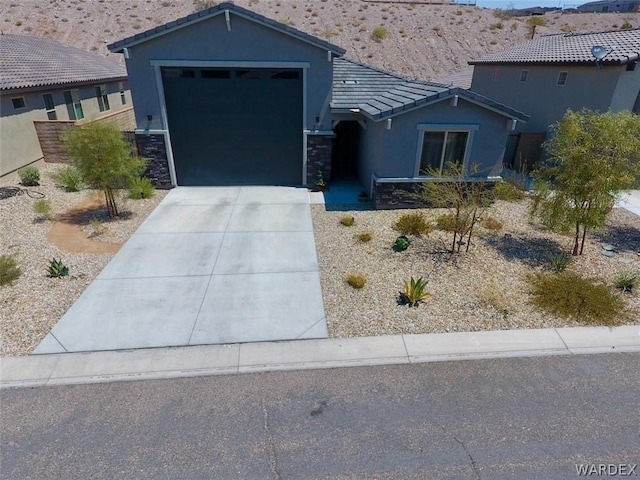 view of front of property with driveway, stone siding, a tile roof, an attached garage, and stucco siding