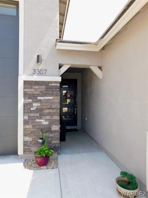 view of exterior entry featuring a garage, stone siding, and stucco siding