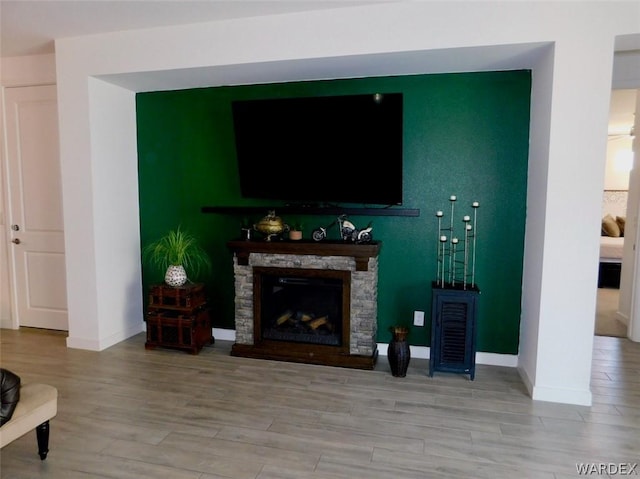 living room with light wood-style flooring, baseboards, and a stone fireplace