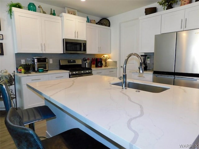 kitchen with light stone counters, stainless steel appliances, a sink, white cabinetry, and a kitchen breakfast bar