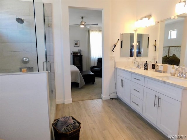 full bath featuring connected bathroom, a stall shower, a sink, and wood finished floors