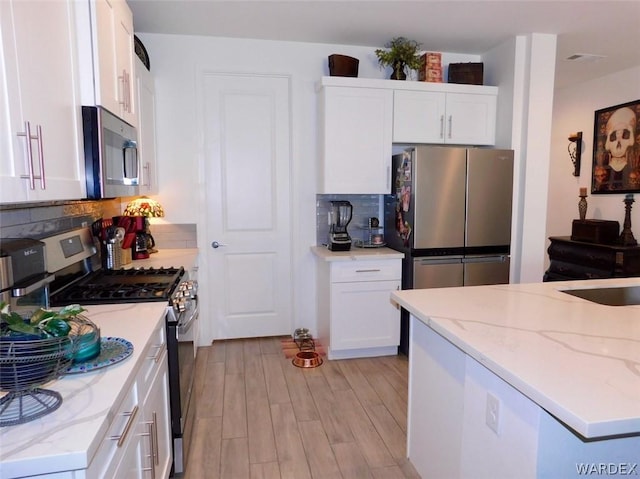 kitchen with decorative backsplash, light stone countertops, stainless steel appliances, light wood-type flooring, and white cabinetry