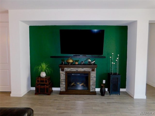 living room featuring baseboards, wood finished floors, and a stone fireplace