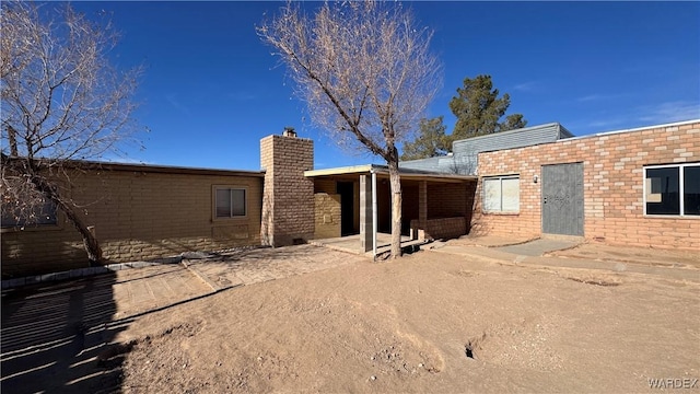 rear view of property featuring brick siding, a chimney, and a patio