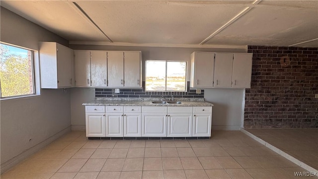 kitchen with white cabinets, a sink, light tile patterned flooring, light stone countertops, and baseboards