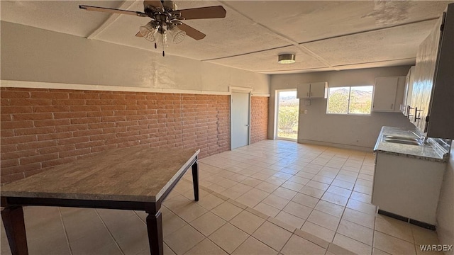 interior space with ceiling fan, a sink, brick wall, and light tile patterned floors