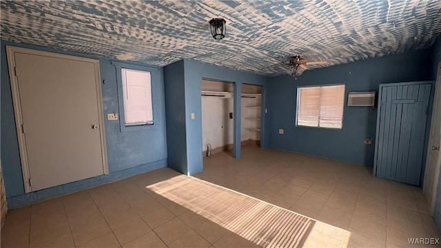 unfurnished bedroom with multiple closets, light tile patterned floors, and a wall mounted AC