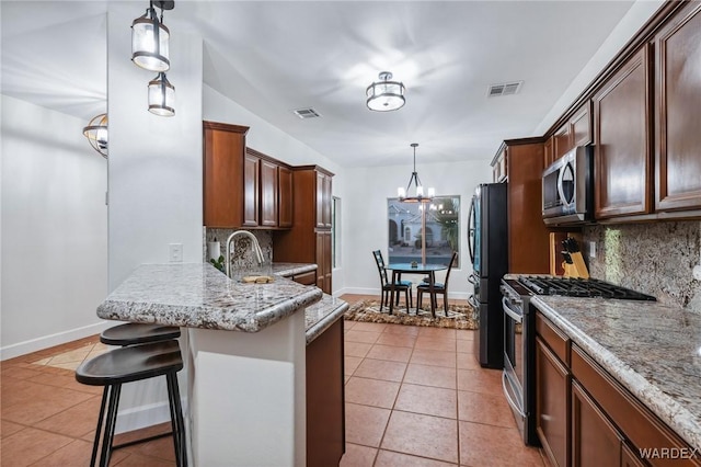 kitchen with stainless steel appliances, hanging light fixtures, a kitchen bar, and visible vents