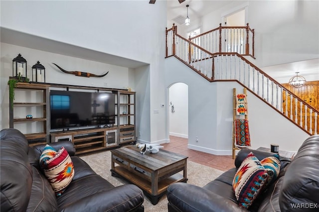 living room with light tile patterned floors, baseboards, arched walkways, a towering ceiling, and stairway