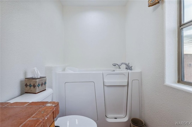 bathroom with a wealth of natural light, a garden tub, and toilet