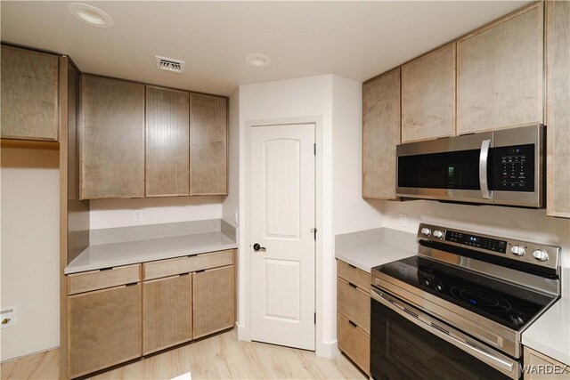 kitchen with appliances with stainless steel finishes, light wood-type flooring, light countertops, and visible vents