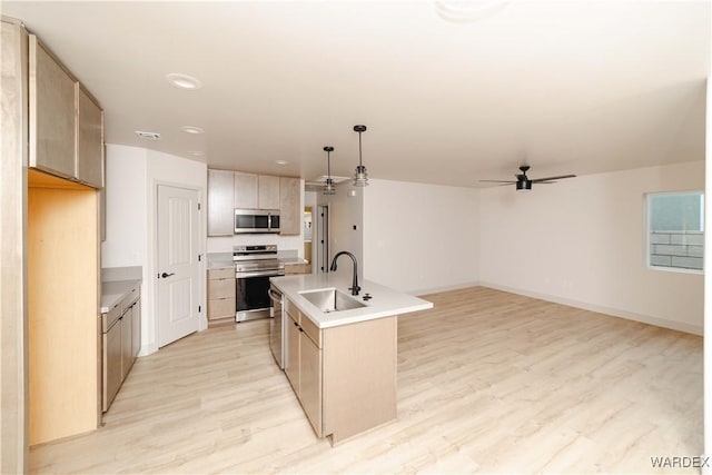 kitchen with stainless steel appliances, light countertops, a center island with sink, and decorative light fixtures