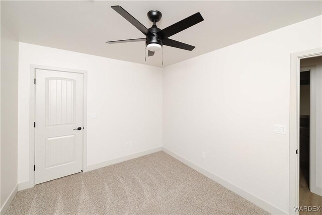 spare room featuring a ceiling fan, light colored carpet, and baseboards