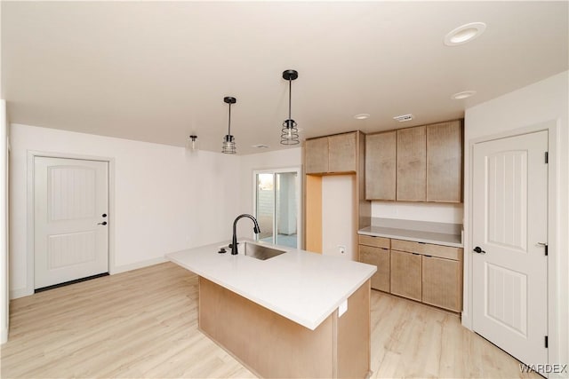 kitchen featuring a sink, light countertops, light wood-type flooring, an island with sink, and decorative light fixtures