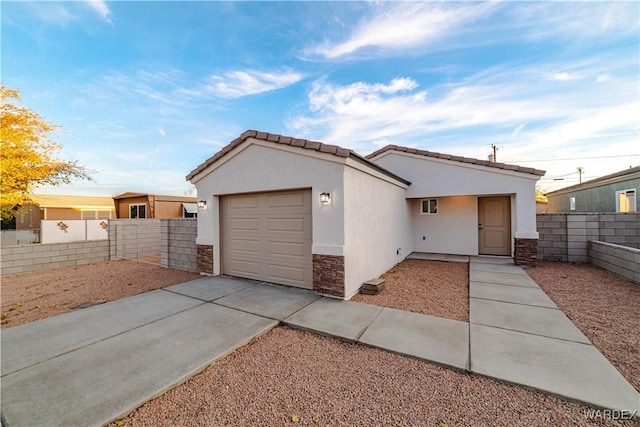 view of front of home featuring driveway, a garage, stone siding, fence, and stucco siding