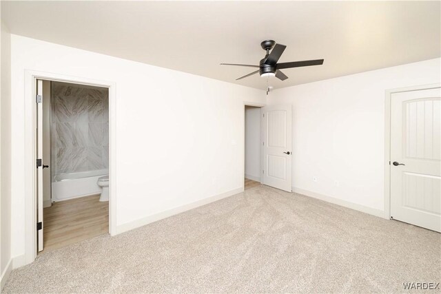 unfurnished bedroom featuring baseboards, ceiling fan, ensuite bathroom, and light colored carpet