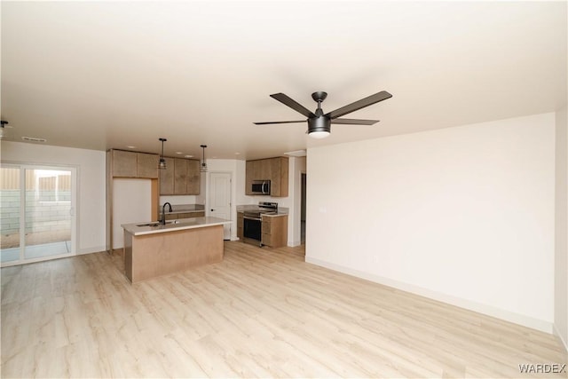 kitchen with a kitchen island with sink, stainless steel appliances, open floor plan, light countertops, and decorative light fixtures