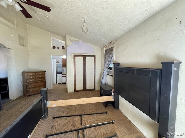 bedroom with ceiling fan, vaulted ceiling, a textured ceiling, and wood finished floors