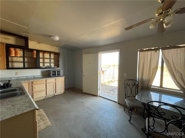 kitchen with ceiling fan, unfinished concrete floors, light countertops, light brown cabinets, and a sink