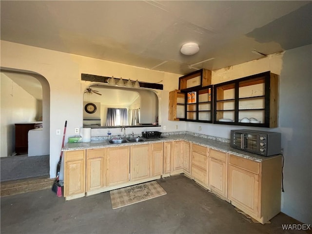 kitchen with a toaster, arched walkways, unfinished concrete floors, light brown cabinets, and a sink