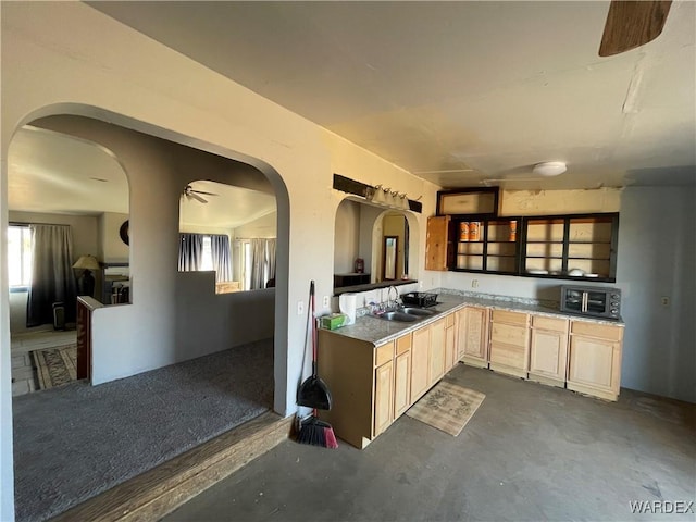 kitchen with arched walkways, light brown cabinets, a sink, a ceiling fan, and unfinished concrete floors