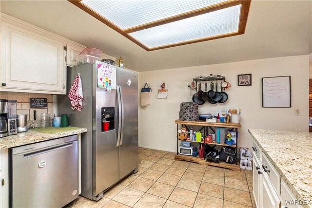 kitchen featuring backsplash, appliances with stainless steel finishes, white cabinetry, light tile patterned flooring, and light stone countertops