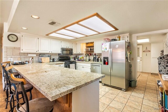 kitchen with light stone counters, stainless steel appliances, visible vents, white cabinets, and a sink