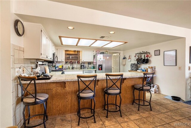 kitchen with appliances with stainless steel finishes, white cabinetry, a peninsula, and a kitchen breakfast bar