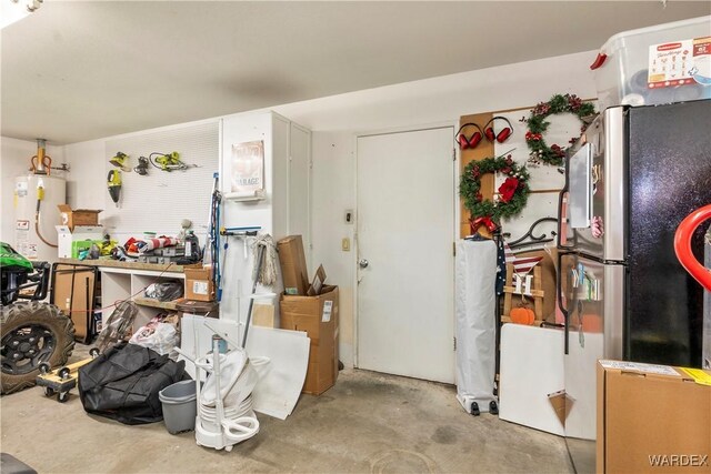 kitchen with unfinished concrete floors, gas water heater, and freestanding refrigerator