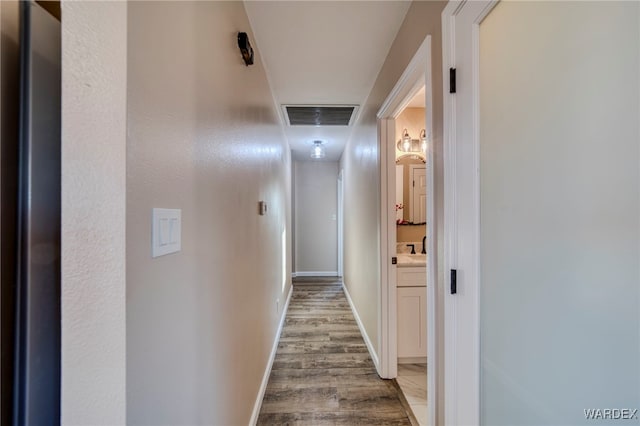 hallway with wood finished floors, visible vents, and baseboards