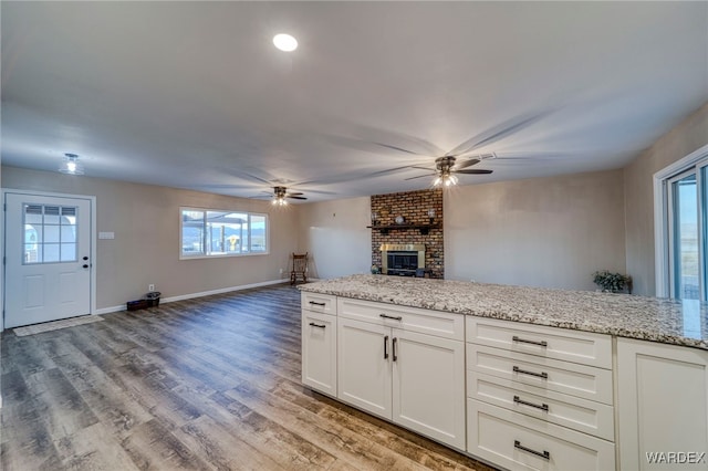 kitchen with baseboards, light stone counters, open floor plan, wood finished floors, and white cabinetry