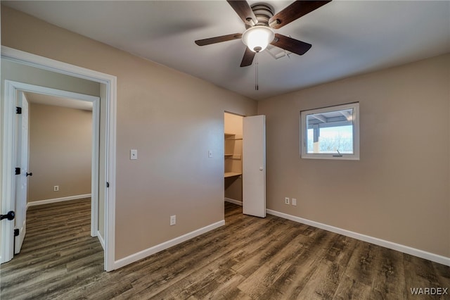 unfurnished bedroom with dark wood-style floors, a spacious closet, baseboards, and a ceiling fan