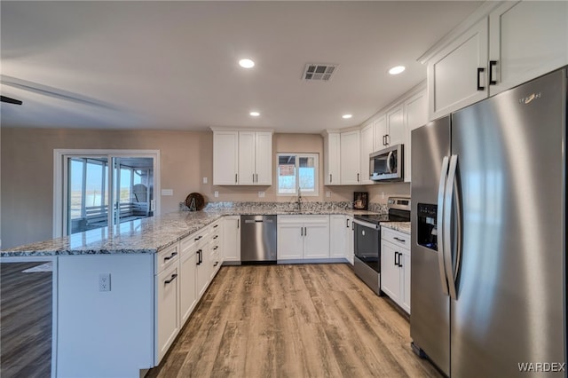 kitchen with a peninsula, visible vents, white cabinetry, appliances with stainless steel finishes, and light stone countertops