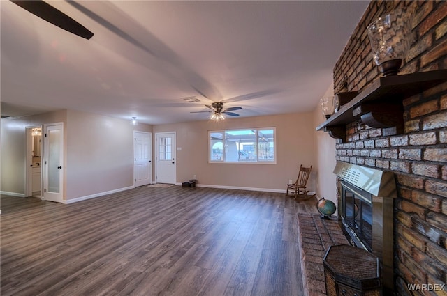 unfurnished living room featuring dark wood-style flooring, a brick fireplace, a ceiling fan, and baseboards