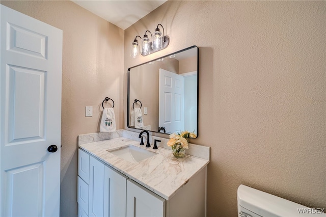 half bathroom with toilet, a textured wall, and vanity