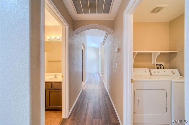 corridor featuring arched walkways, light wood-style flooring, washing machine and clothes dryer, and visible vents