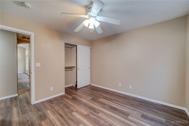 unfurnished bedroom with a closet, arched walkways, dark wood-style flooring, and baseboards