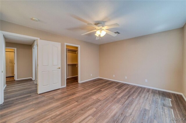 unfurnished bedroom with a closet, a spacious closet, baseboards, and wood finished floors